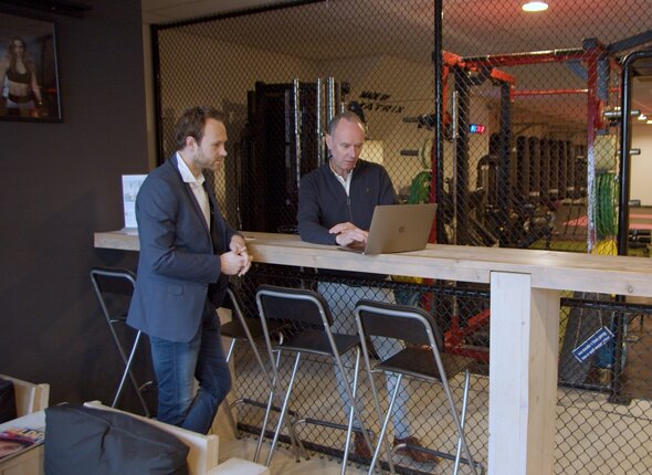Twee mannen aan een statafel kijken naar laptop