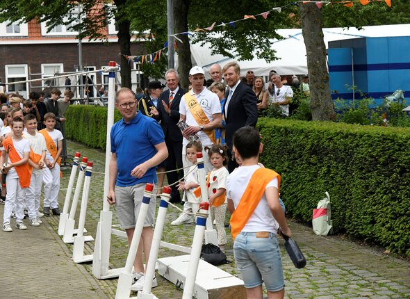 Afbeelding van kinderen die ringsteken onder toeziend oog van de koning en de commissaris