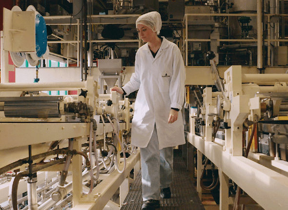 vrouw met haarnetje en witte stofjas bij machine