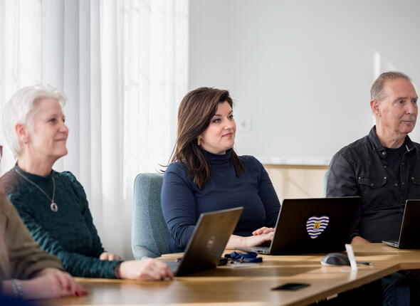 Drie collega's zitten aan een tafel in een vergaderruimte en kijken dezelfde kant op.