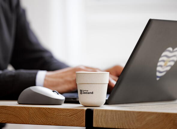 Een koffiebeker naast een laptop op een bureau.