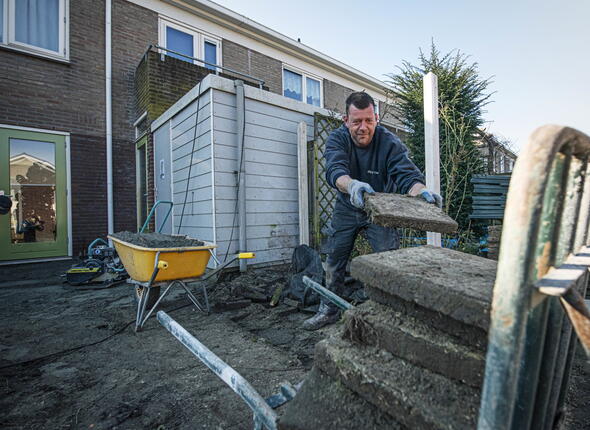 Een man haalt tegels uit een tuin om plaats te maken voor groen.