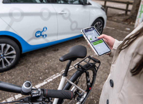 Een fietser met smartphone boekt een deelauto
