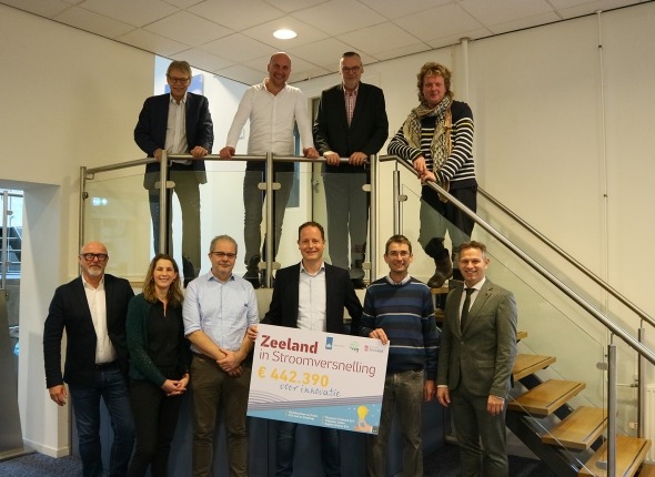 Een groepsfoto van subsidieontvangers van Zeeland in Stroomversnelling-subsidie. Vier mensen staan bovenop de trap. Een zestal staan onderaan de trap en houden een foambord vast met daarop 'Zeeland in Stroomversnelling €442.390 voor innovatie'. 
