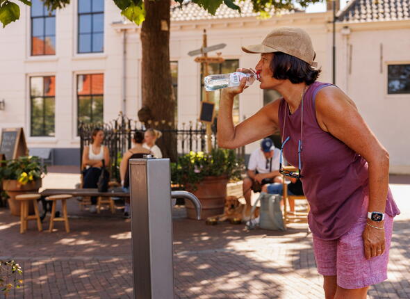 Een vrouw drinkt water uit een flesje dat ze net heeft gevuld bij een drinkwatertappunt in Zierikzee.