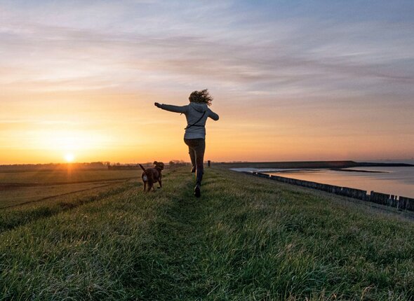 Vrouw met hond rent over dijk bij zonsondergang