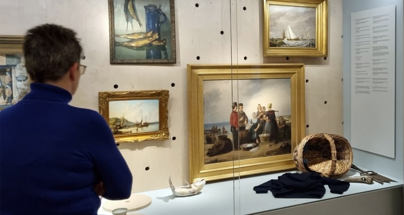 Vrouw bekijkt schilderijen en voorwerpen in vitrine
