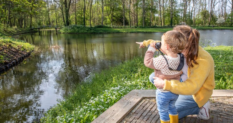 Moeder en kind met verrekijker kijken uit over water in Landgoed Ter Hooge
