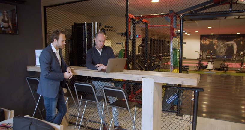 Twee mannen aan een statafel kijken naar laptop