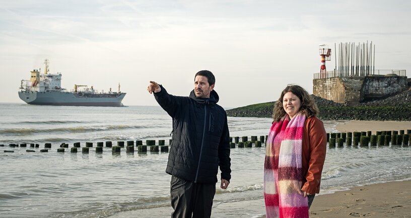 Twee mensen staan aan de waterkant en wijzen naar iets in de verte