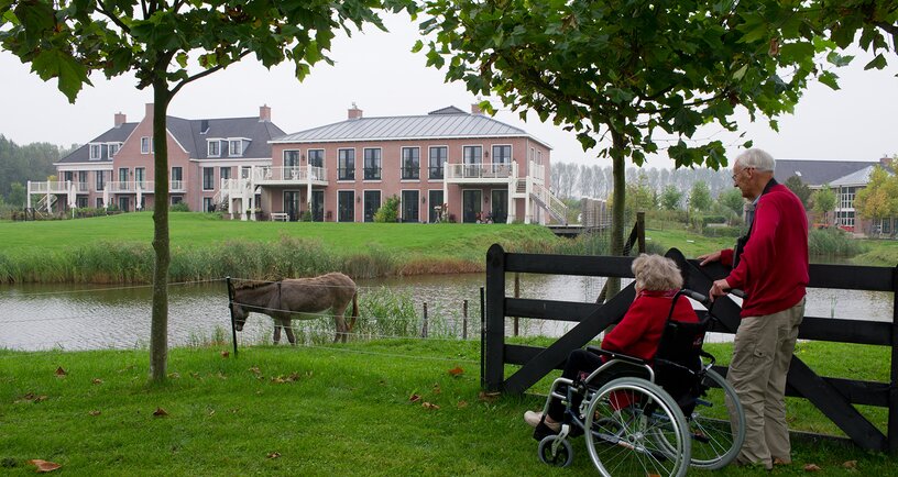 Man met vrouw in rolstoel kijken naar Zorghotel Geersdijk