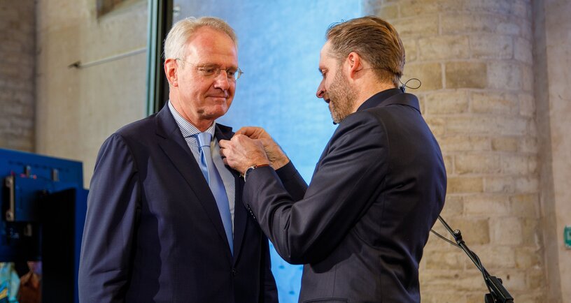 Foto van De Jonge die Polman de onderscheiding opspeldt