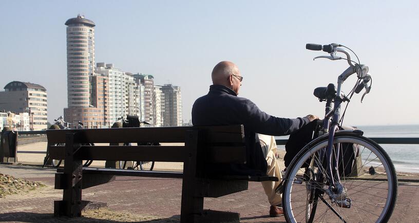 Man zit op bankje op de Boulevard met zijn hand op zijn fiets.