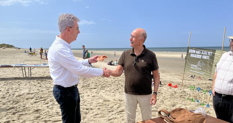 Gedeputeerde Van der Maas neemt de schenking van Jeroen van den Brande in ontvangst tijdens de Nationale Archeologiedagen 2025