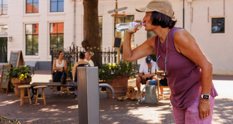 Een vrouw drinkt water uit een flesje dat ze net heeft gevuld bij een drinkwatertappunt in Zierikzee.