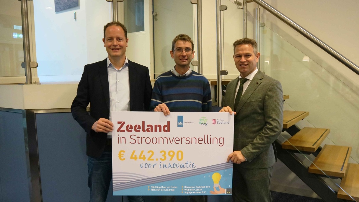 Twee projecteigenaren van Gewasbescherming door robotisering houden samen met gedeputeerde Jo-Annes de Bat een foambord vast met daarop 'Zeeland in Stroomversnelling €442.390 voor innovatie'. 