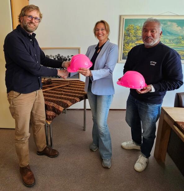 Edwin Prins overhandigt twee roze bouwhelmen van de Wonen & Zorg Kennis Karavaan aan Roos Antheunisse en Bobbe Lilipaly